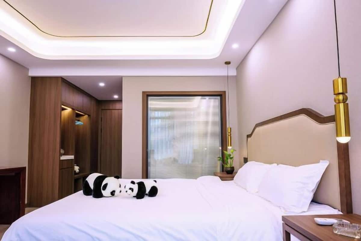 Habitación de hotel con cama, mesita de noche, lámpara y un peluche de panda.