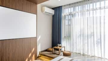 A modern hotel room with a large window, a flat-screen TV, and a small table with a lamp.