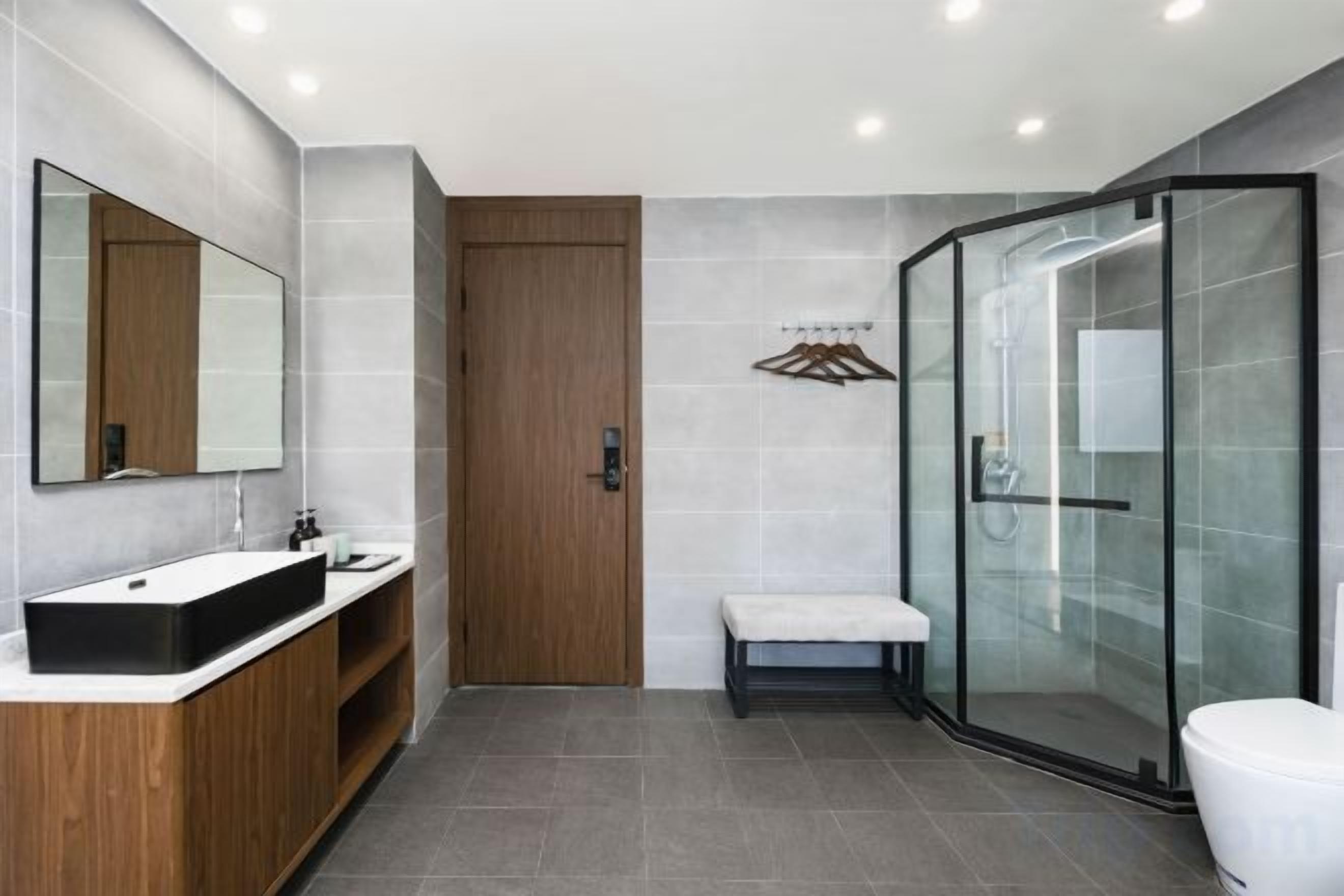 Un baño moderno con cabina de ducha de vidrio, tocador de madera y un banco.