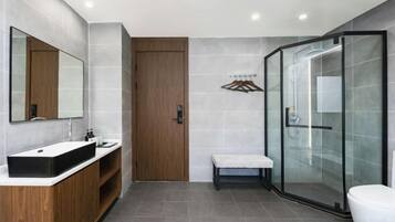 Un baño moderno con cabina de ducha de vidrio, tocador de madera y un banco.