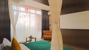 Une chambre d’hôtel avec un lit, une moquette verte, une petite table, une chaise et une grande fenêtre avec des rideaux.