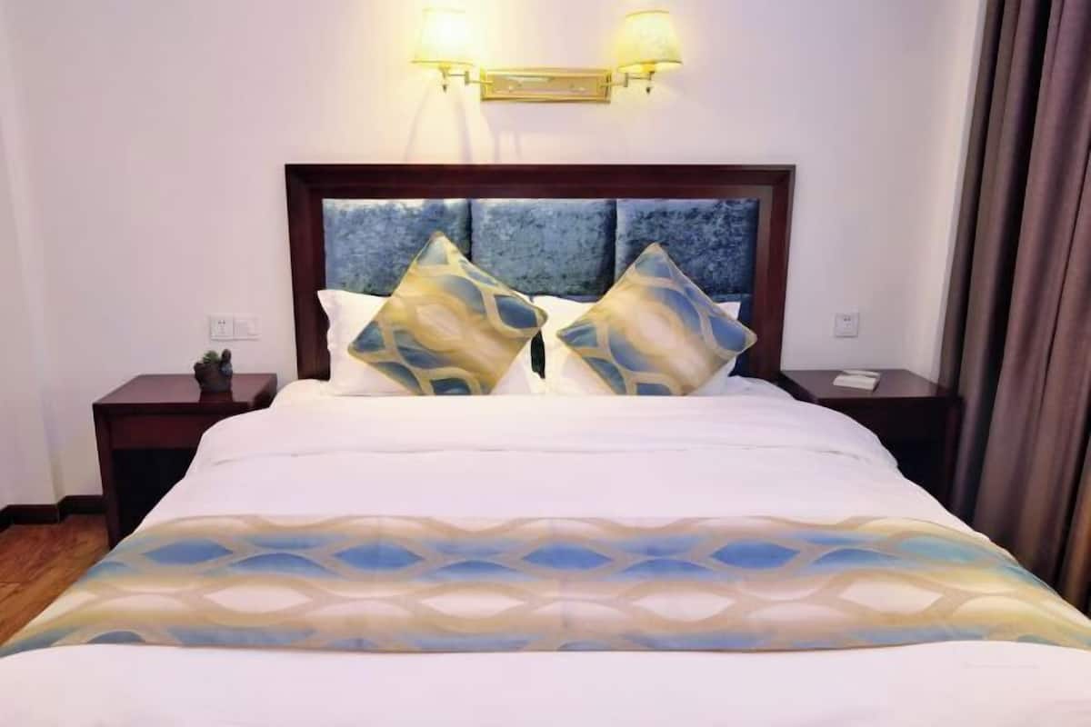 Habitación de hotel con cama, dos mesitas de noche, cabecero con apliques de pared y vistas al exterior.