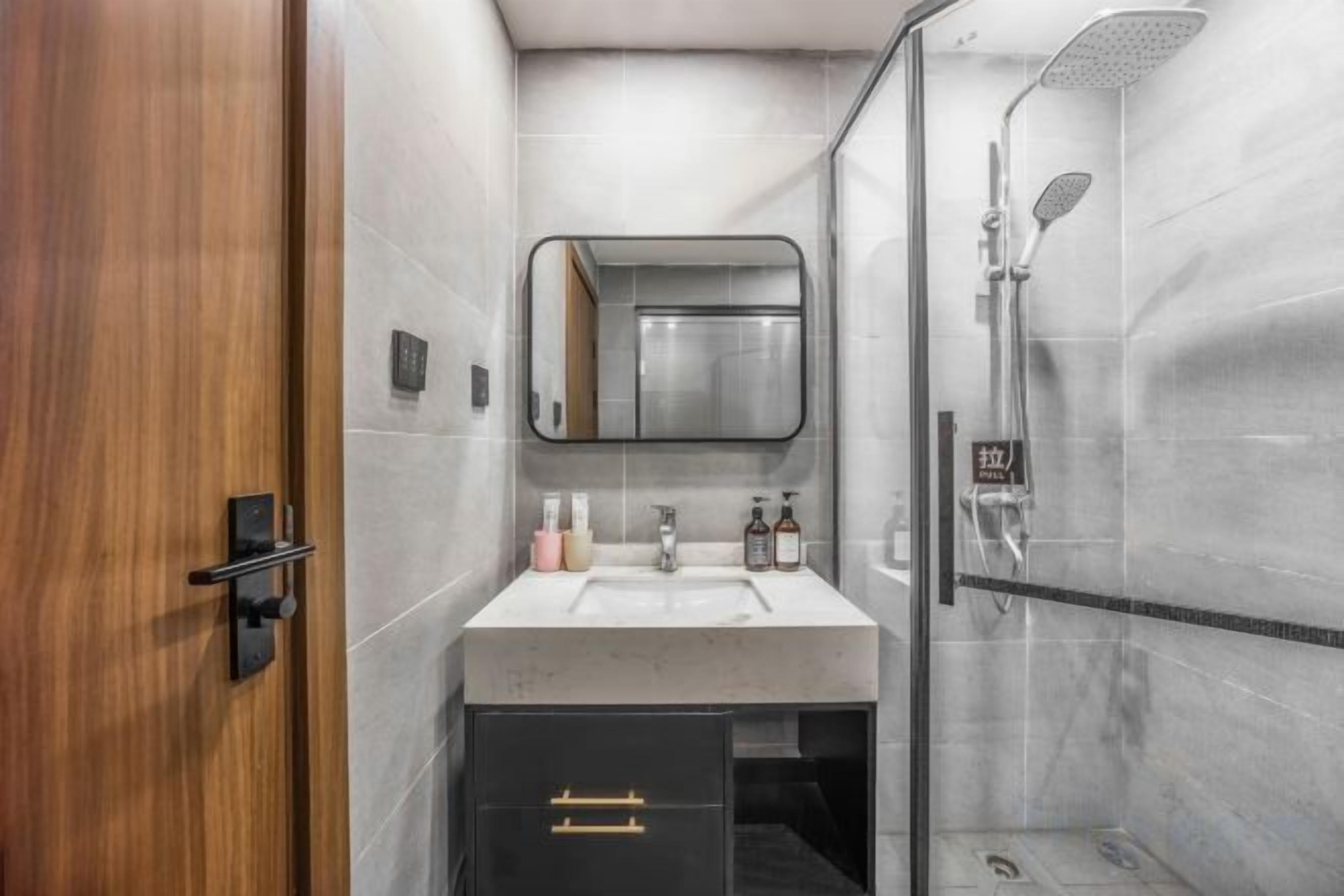 Un baño con puerta de madera, un espejo, un lavabo con artículos de aseo y una zona de ducha.