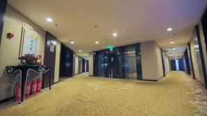 Un couloir d’hôtel avec un revêtement de sol en moquette, un comptoir de réception agrémenté d’un arrangement floral et un extincteur.