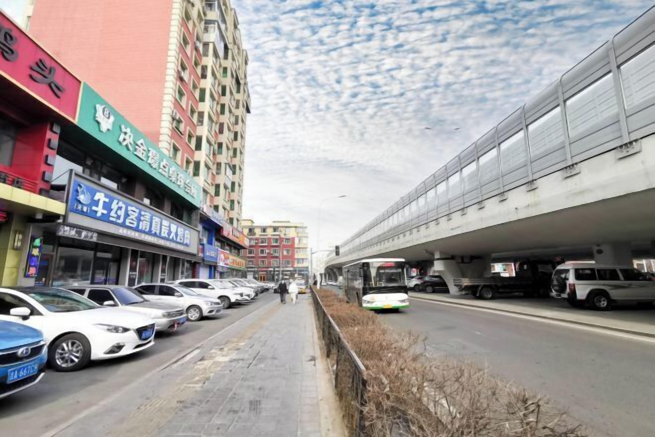 A street scene with parked cars, a pedestrian walkway, and a train on an elevated track.