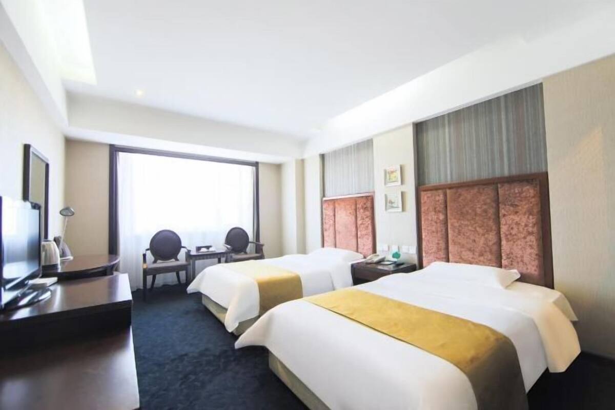 A hotel room with two beds, a desk, a chair, a TV, and a large window.