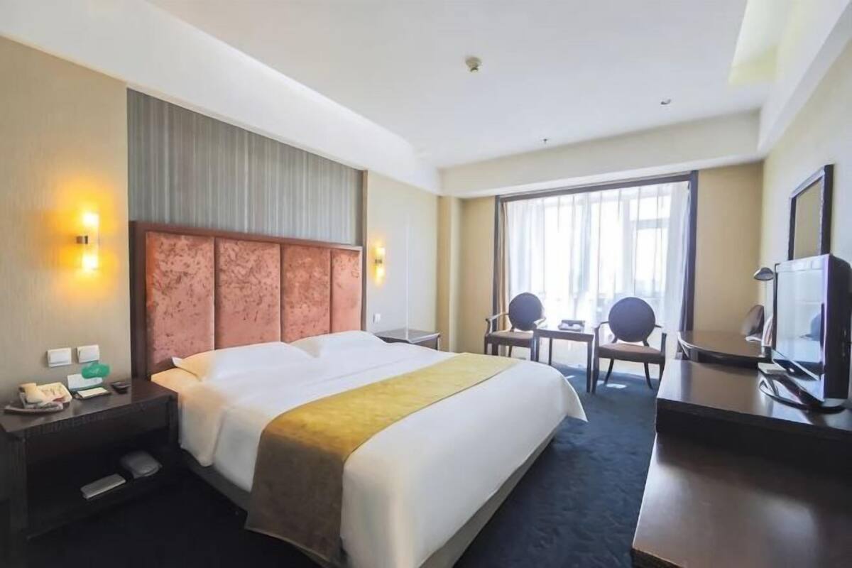 A hotel room with a large bed, bedside tables, a desk, a chair, a television, and a window with curtains.