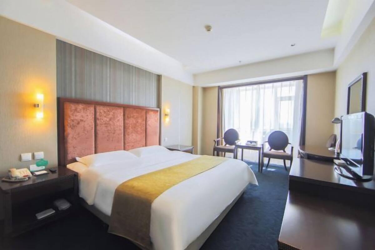 A hotel room with a large bed, a desk with a chair, a television, and a window with curtains.