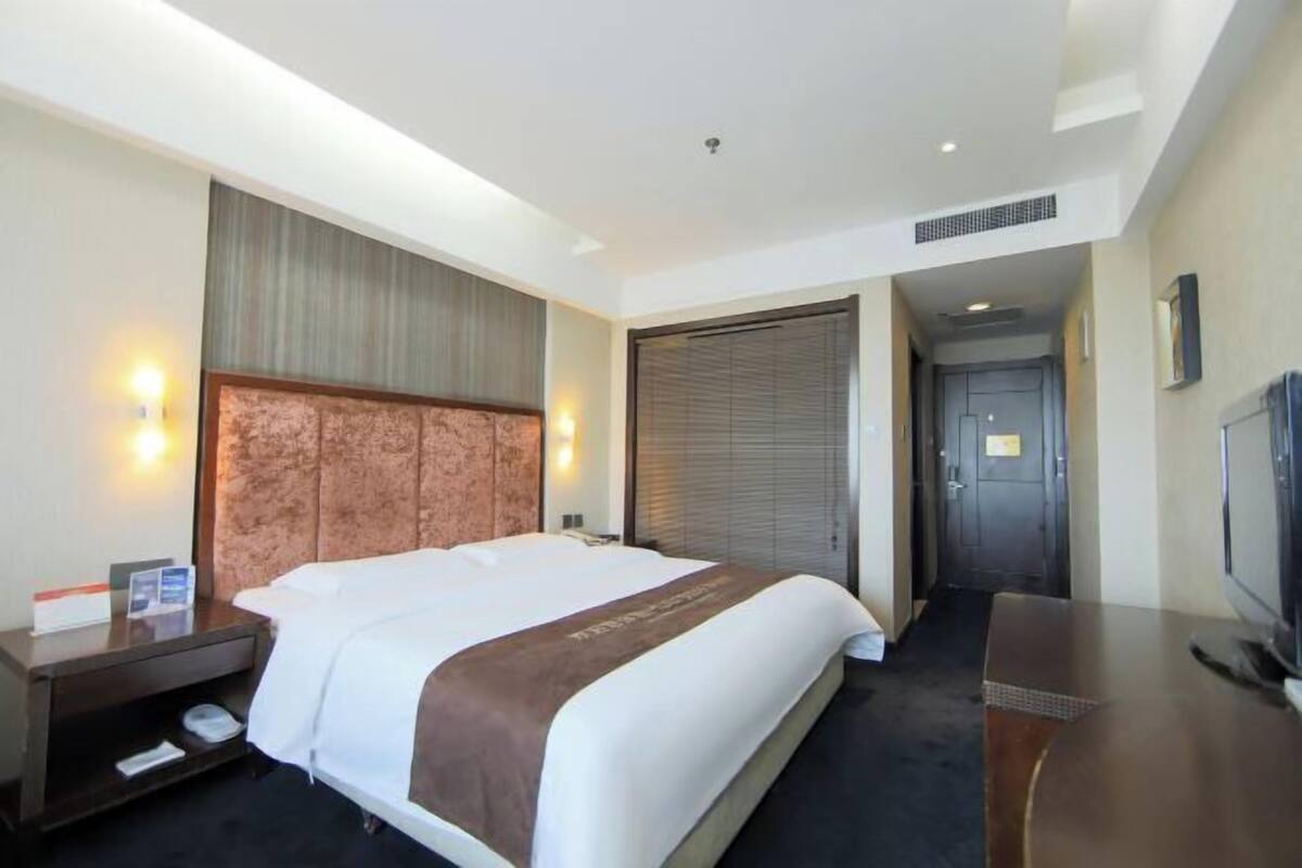 A hotel room with a large bed, a bedside table with a lamp, a flat-screen TV, and a wardrobe.