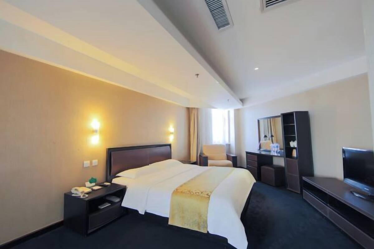 A hotel room with a bed, bedside tables, a TV, and a wardrobe.