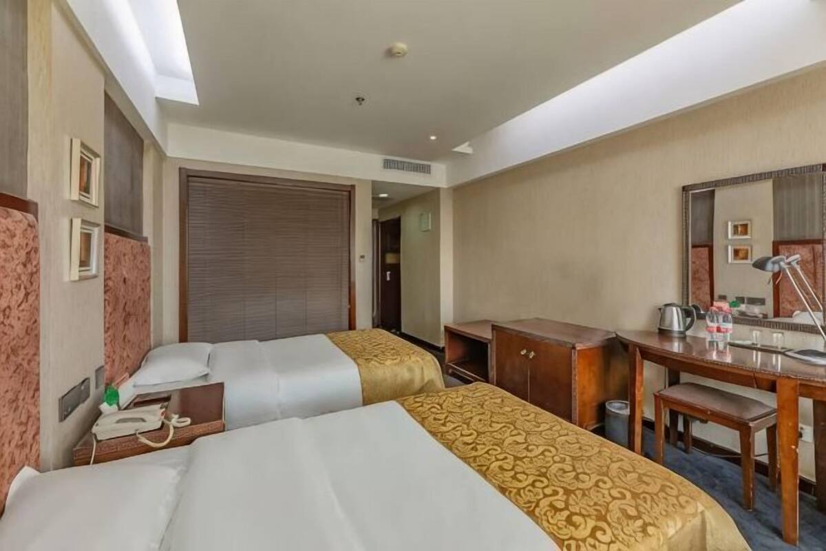 A hotel room with two beds, a desk, a chair, a mirror, and a wardrobe.