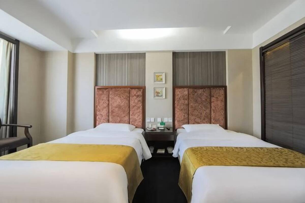 A hotel room with two beds, a desk, a chair, and a window with curtains.