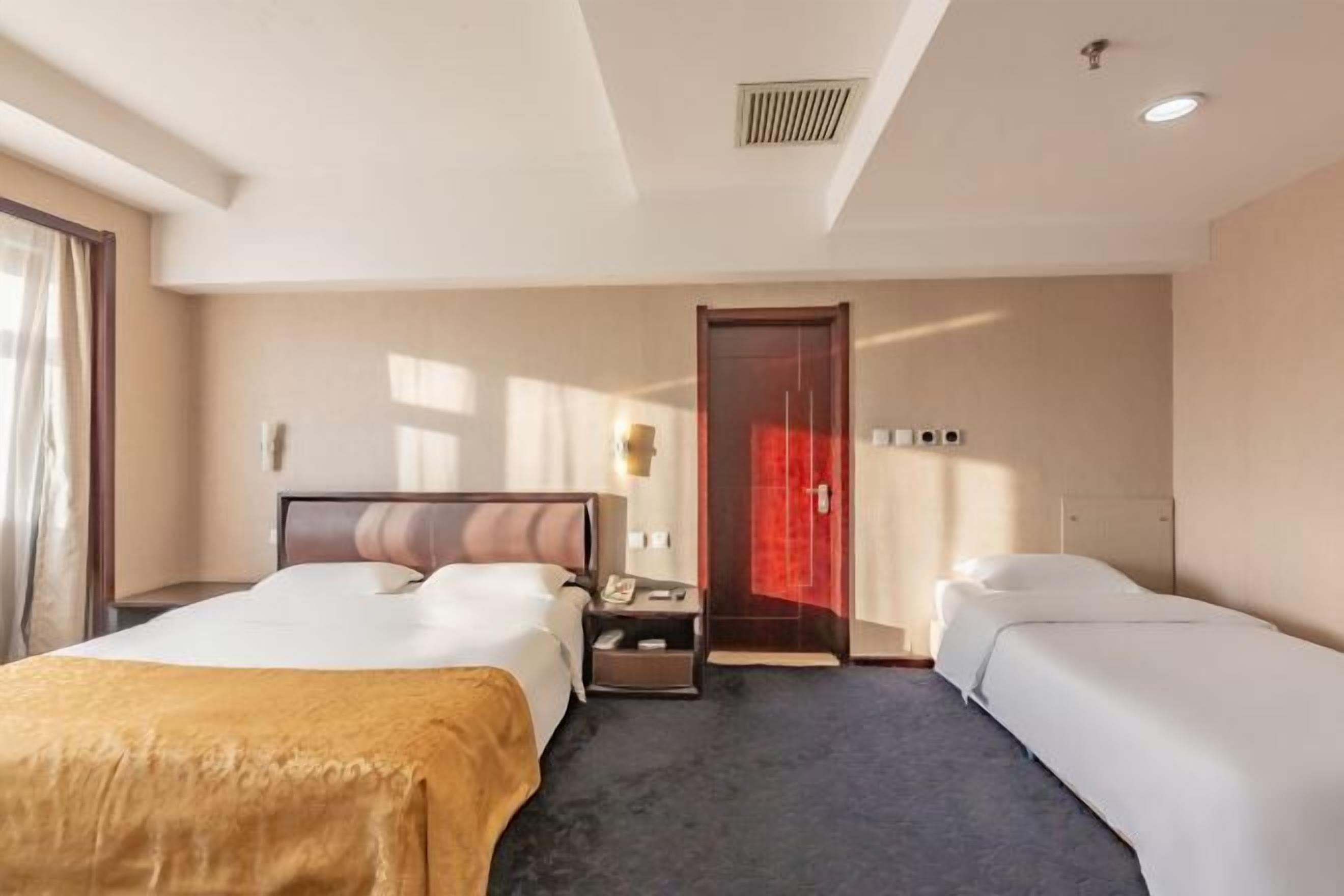 A hotel room with two beds, a nightstand, a red door, and a window with curtains.
