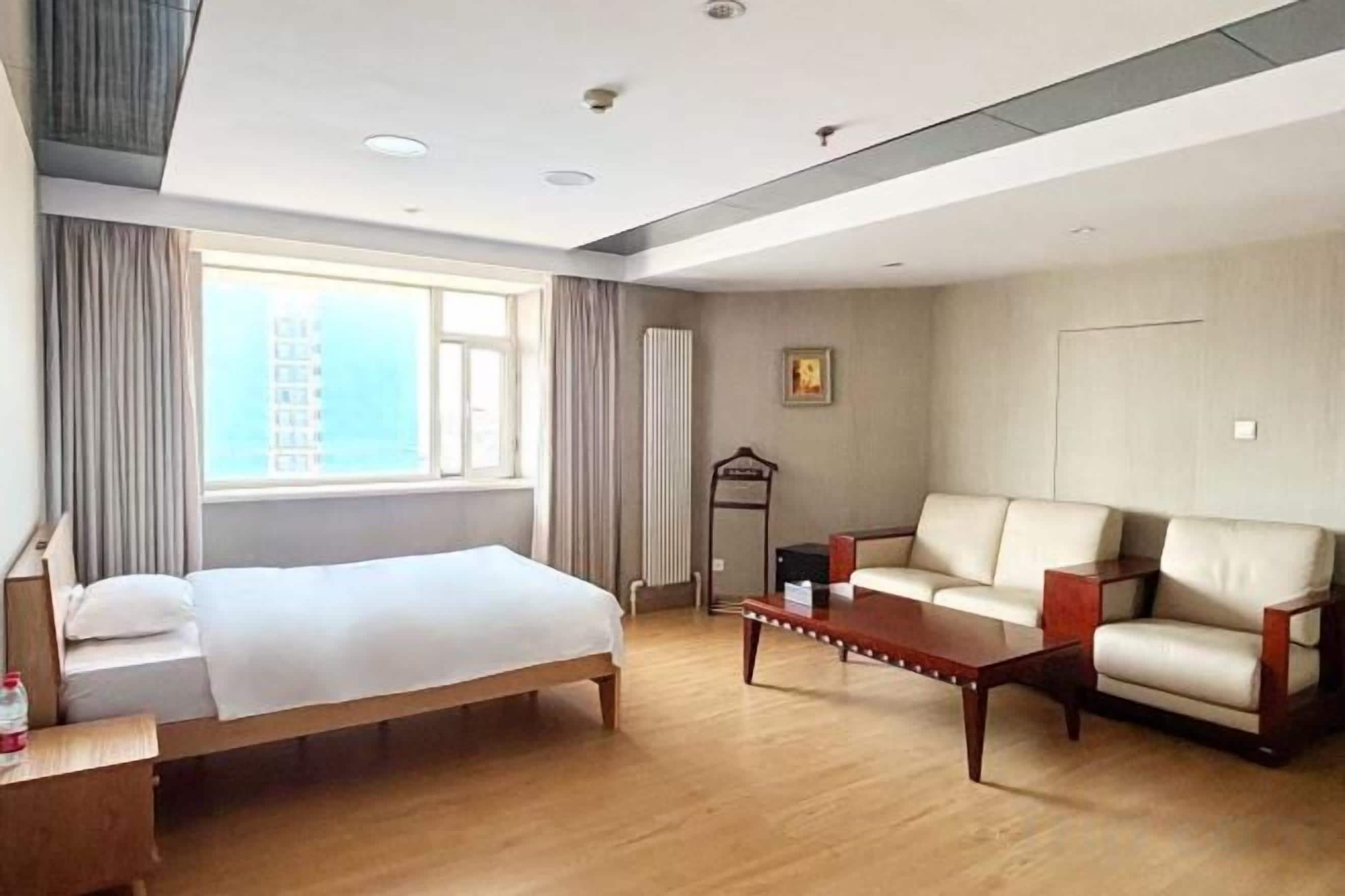 A hotel room with a bed, a sofa, a coffee table, and a window with curtains.