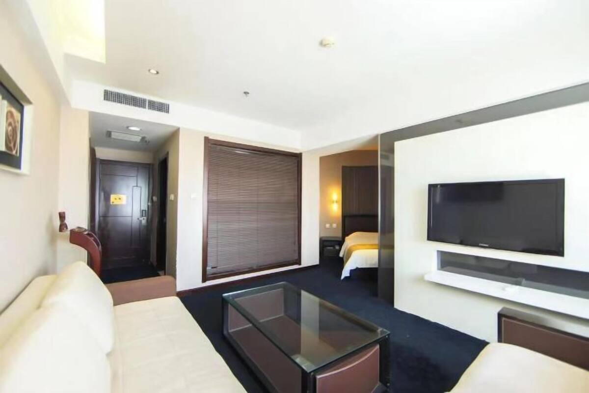 A hotel room with a bed, a TV, a sofa, and a glass coffee table.