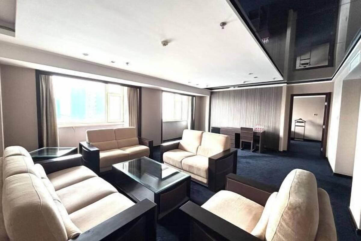 A modern hotel room with a living area featuring sofas, a coffee table, and a dining area with a table and chairs.