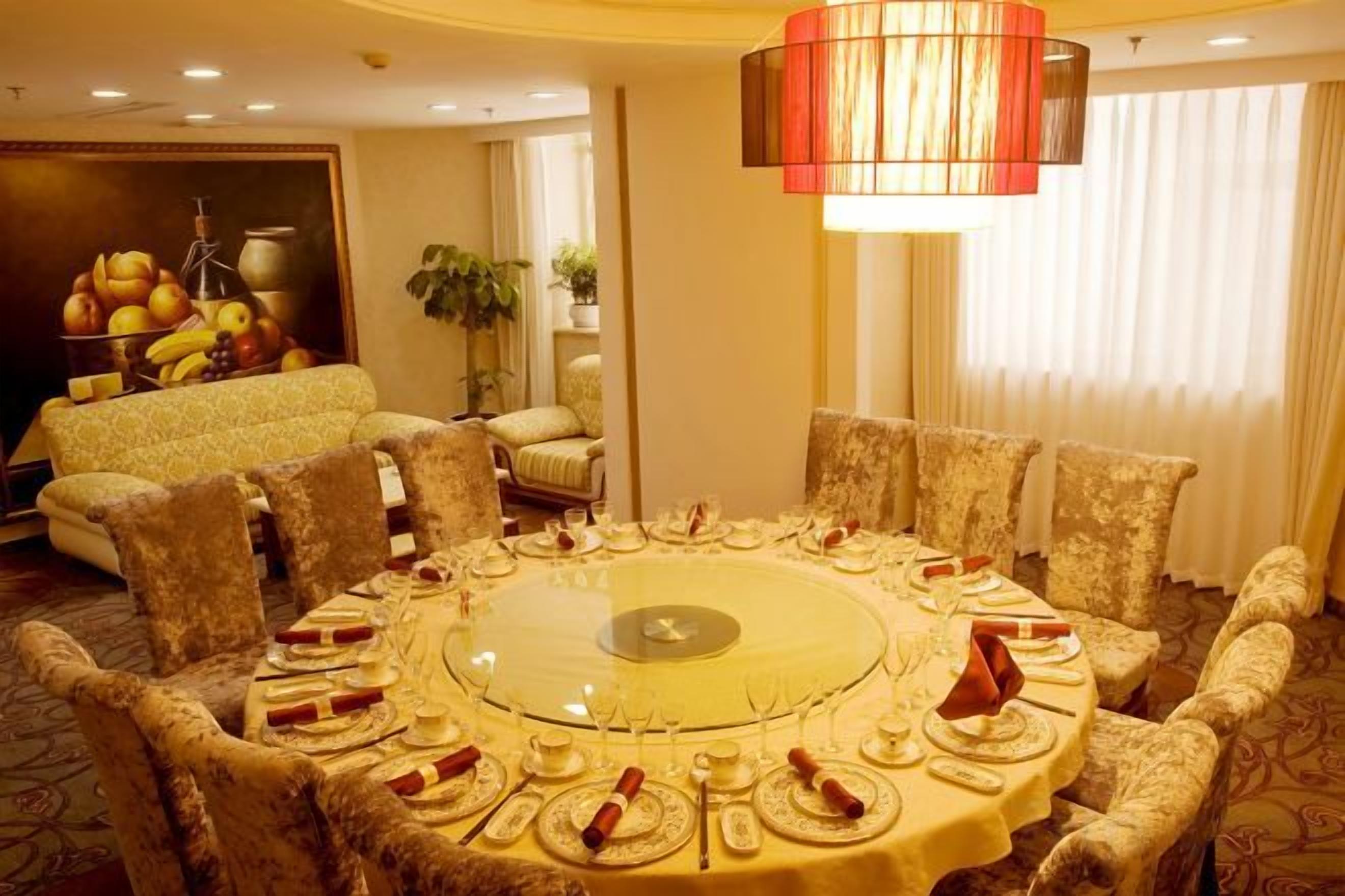 A round dining table with chairs, a chandelier, and a fruit display in the background.