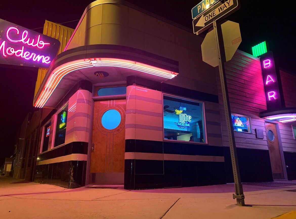 A Club Moderne with neon signage, a bar, and a one-way street sign.