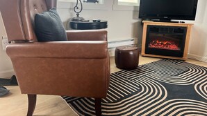 Ein Wohnzimmer mit Ledersessel, schwarzem Fernseher, Kamin und Teppich mit Muster.