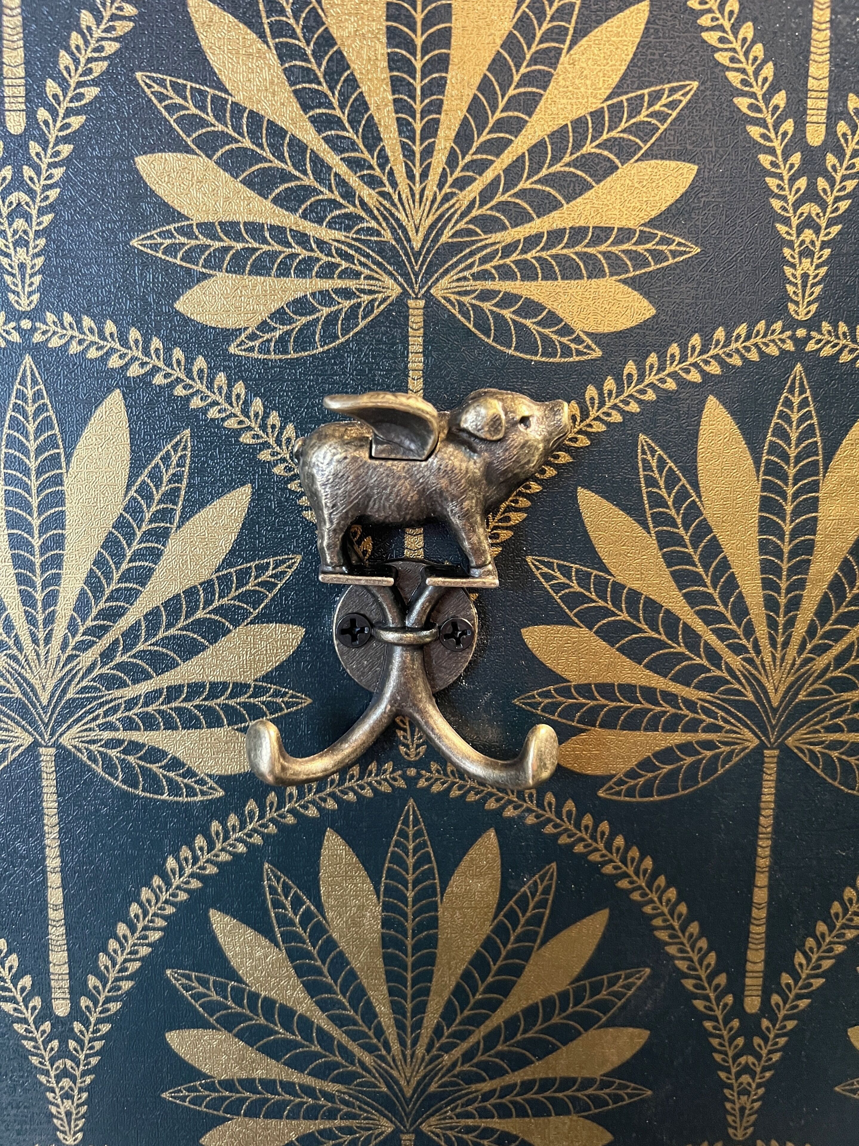 Een decoratieve metalen grendel met een varken als versiering op een oppervlak met structuur.