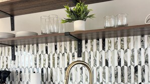 Eine Küche mit einem schwarzen Spülbecken, einem goldenen Wasserhahn und einer Marmor-Spritzschutzwand.