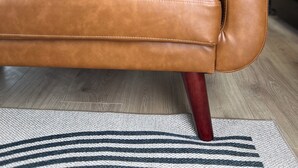 Een bruine leren bank met een donkergrijs kussen in een moderne keuken met houten vloeren en een gestreept vloerkleed.