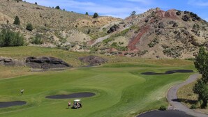 Een golfbaan met een helder uitzicht op de green, bunkers en een heuvelachtig landschap op de achtergrond.
