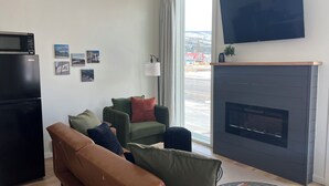 Een moderne woonkamer met een flatscreen televisie, een open haard, een bank en een eethoek met een zwarte koelkast.