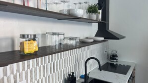 Een moderne keuken met een witte betegelde spatwand, een zwarte afzuigkap en een RVS spoelbak.