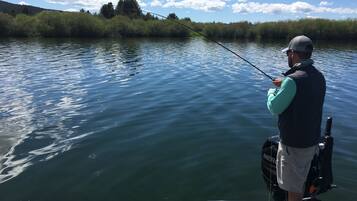 Une personne est en train de pêcher sur un bateau, l’eau est calme et une côte boisée se dessine à l’arrière-plan.