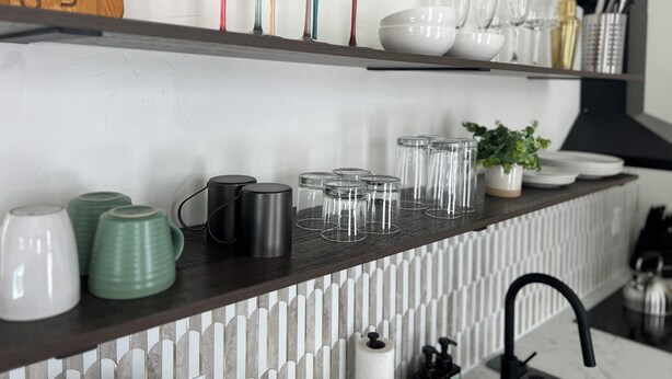 Een aanrecht met diverse glazen, waaronder wijnglazen en tumblers, en een klok aan de muur.