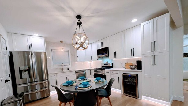 A modern kitchen with white cabinets, a stainless steel refrigerator, a microwave, and a dining table with chairs. - 10 Burnett Home (Rome)