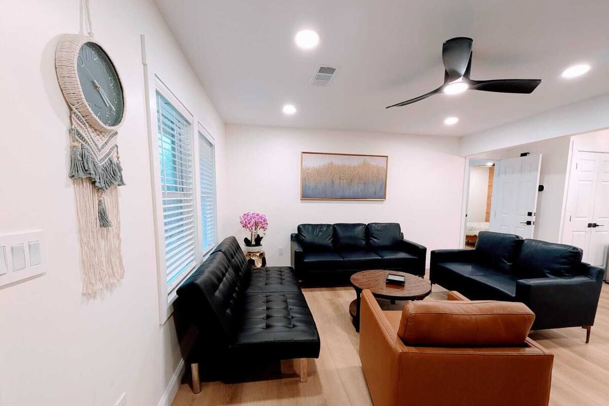 A modern living room with a black leather sofa, a brown leather armchair, a round coffee table, and a macrame wall hanging.