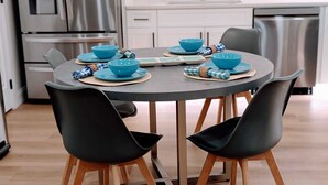 A modern kitchen with a round table set for four, featuring blue bowls and plates, black chairs, and a stainless steel refrigerator. - 10 Burnett Home (Rome)