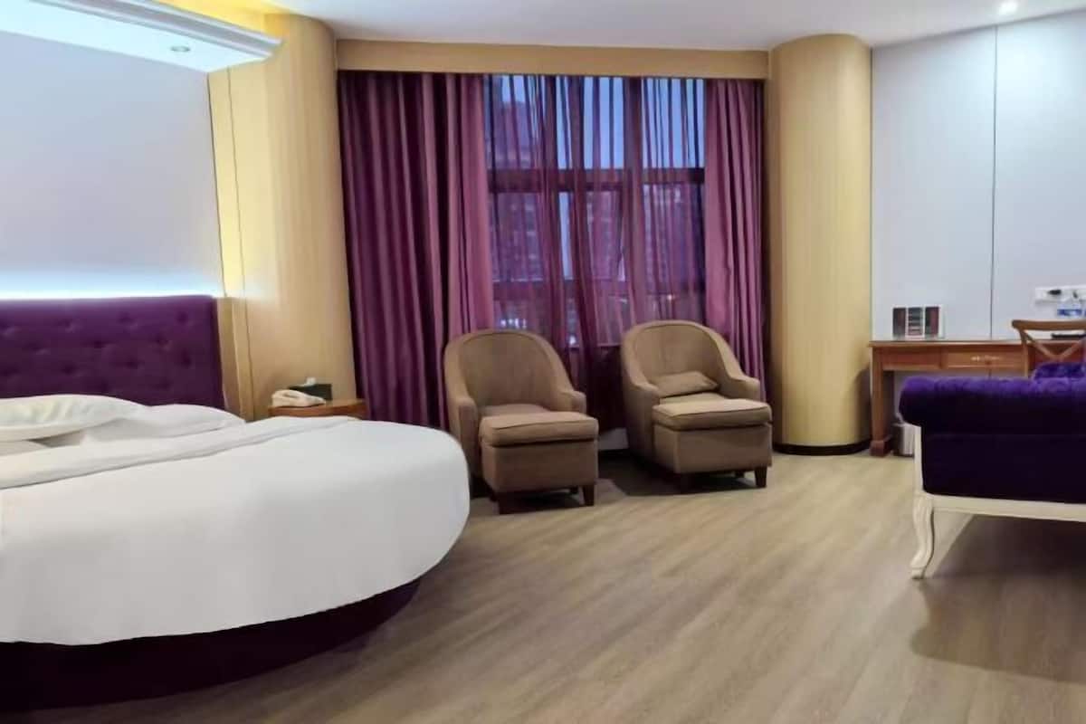 A hotel room with a bed, two armchairs, a desk, and a purple sofa.