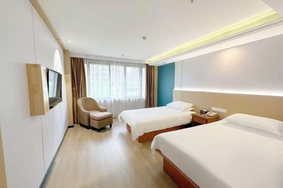A hotel room with two beds, a TV mounted on the wall, a chair, and a bedside table with a phone.