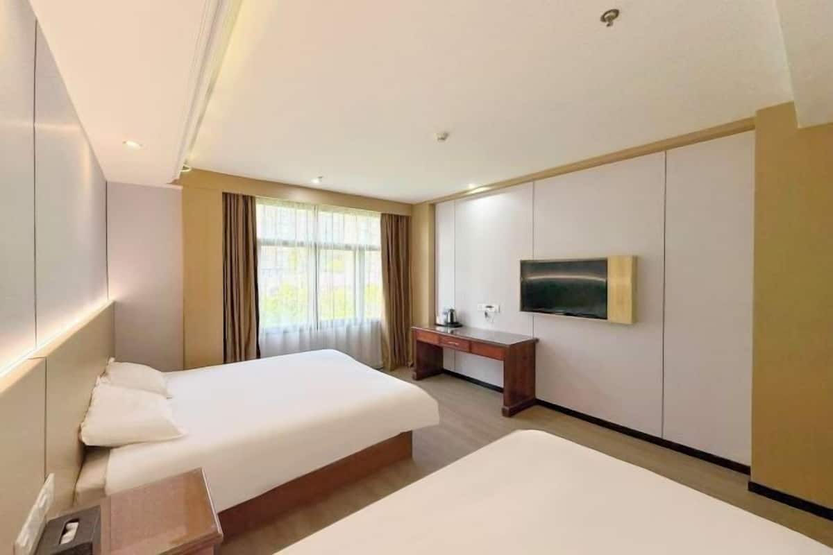 A hotel room with two beds, a desk, a TV, and a window with curtains.