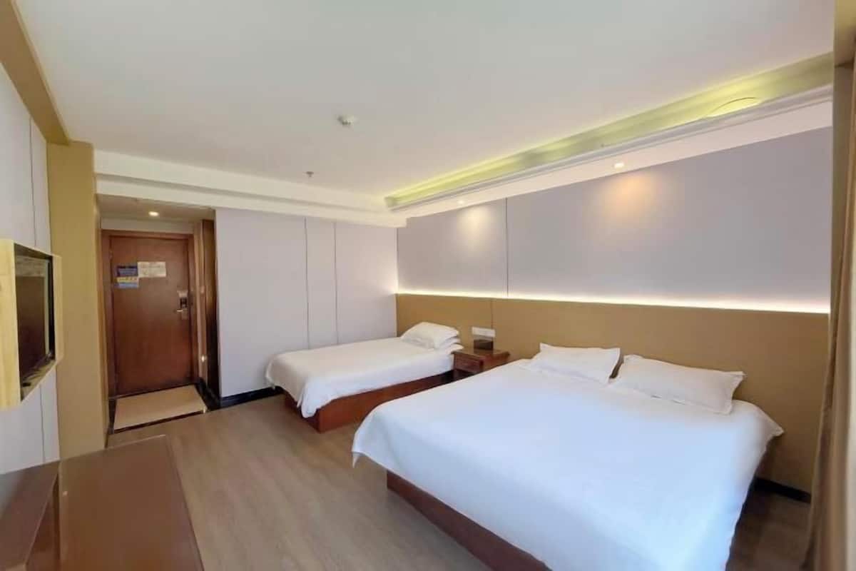 A hotel room with two beds, a wooden floor, a flat-screen TV, and a door leading to another room.