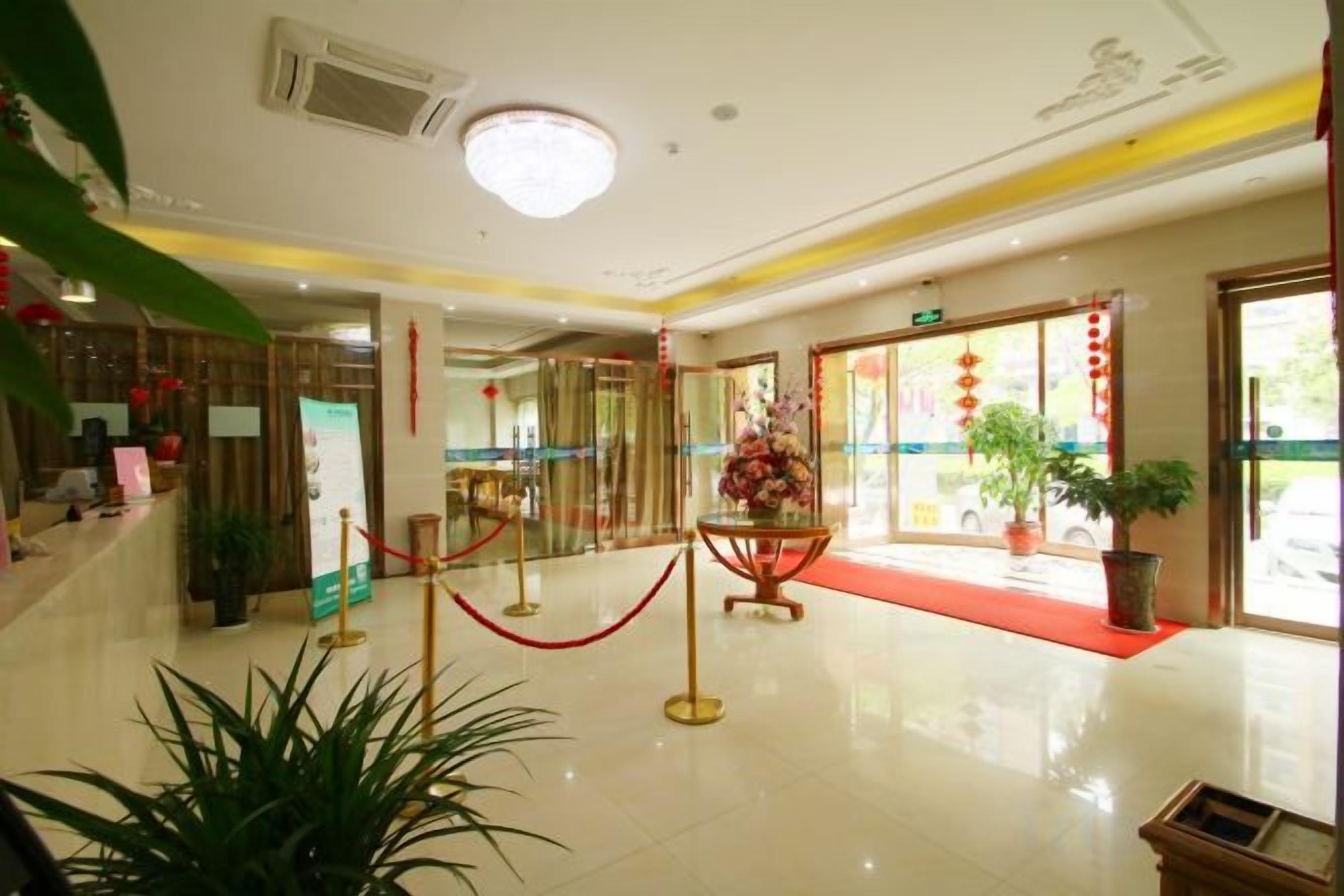 A hotel lobby with a red carpet, potted plants, and a reception desk.