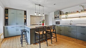 Una cocina moderna con armarios grises, una isla de madera con taburetes tipo barra, luces colgantes y un salpicadero con un diseño geométrico.