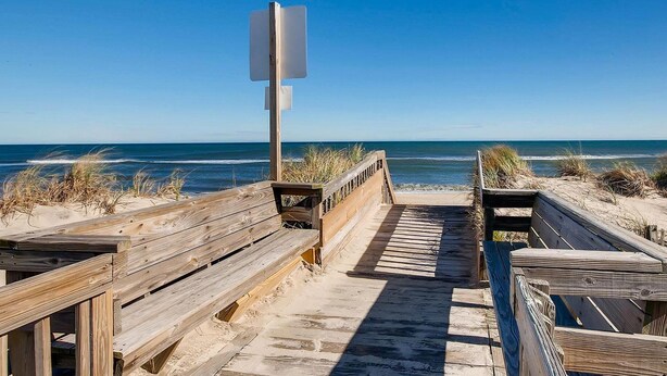 Un paseo marítimo de madera que lleva a la playa, con un poste de señalización vacío.