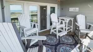 Un espacio al aire libre techado con sillas Adirondack blancas, una pequeña mesa y un ventilador de techo.