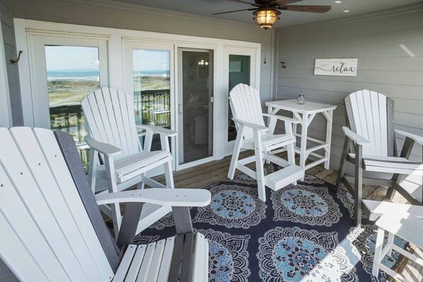 A covered outdoor area with white Adirondack chairs, a small table, and a ceiling fan.