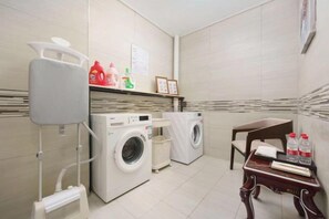 A laundry area with two washing machines, a drying rack, and a table with bottles.