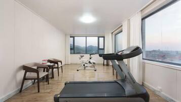 A room with a treadmill, a desk, chairs, and a large window with a view.