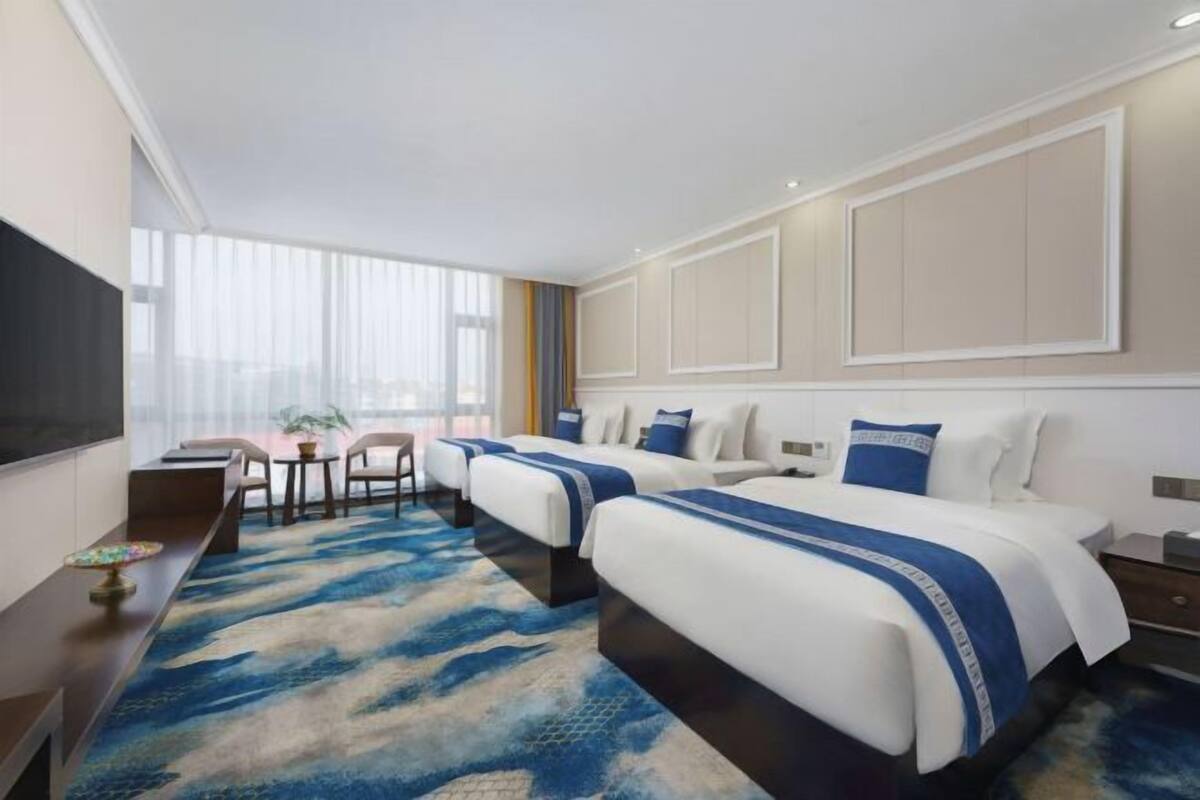 Habitación de hotel con dos camas, televisión, escritorio y vista a la ciudad.