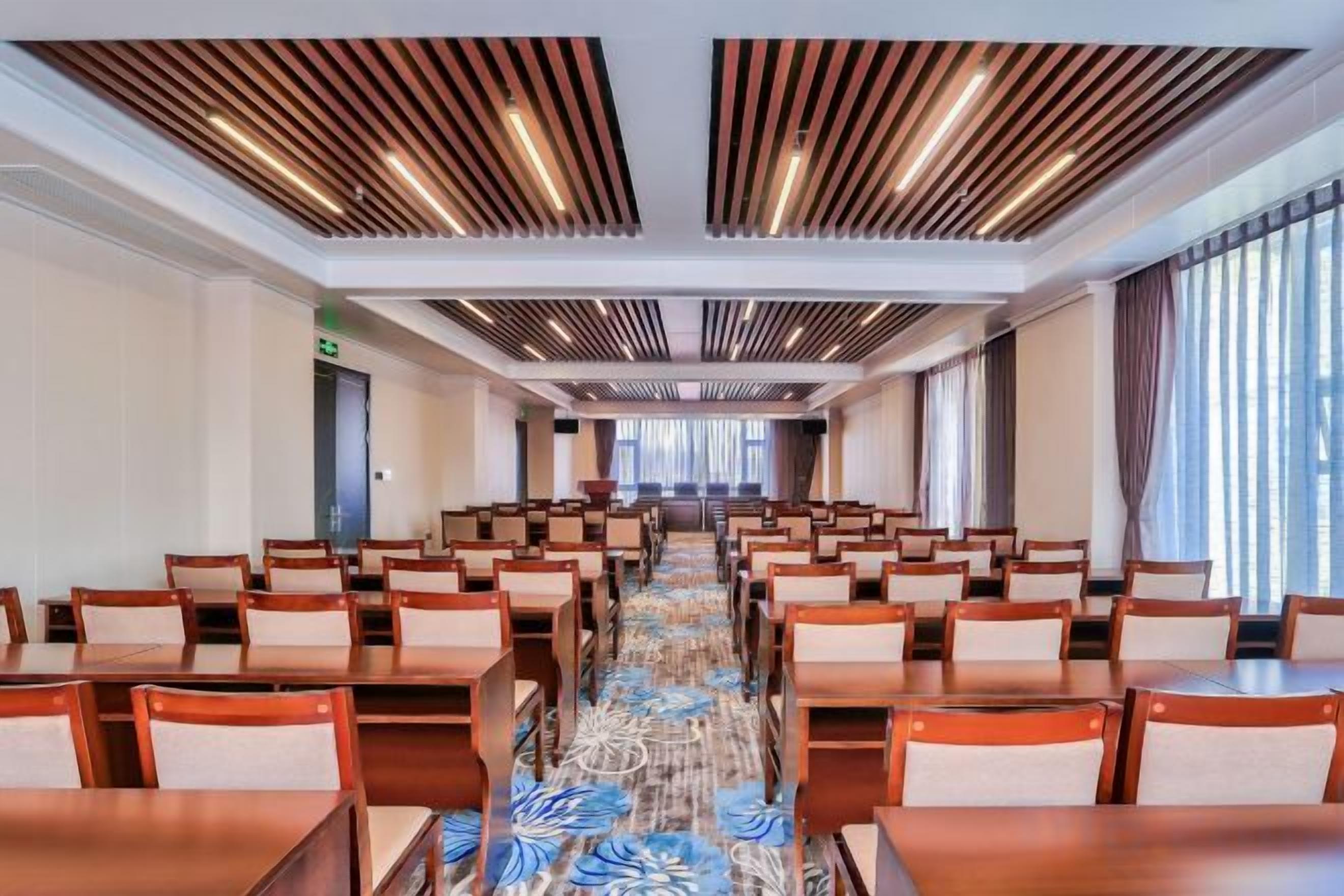 A hotel conference room with rows of tables and chairs, a patterned carpet, and a modern ceiling design.