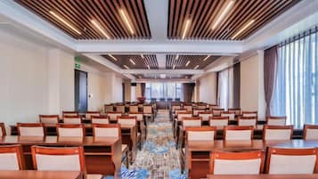 A hotel conference room with rows of tables and chairs, a patterned carpet, and a modern ceiling design.