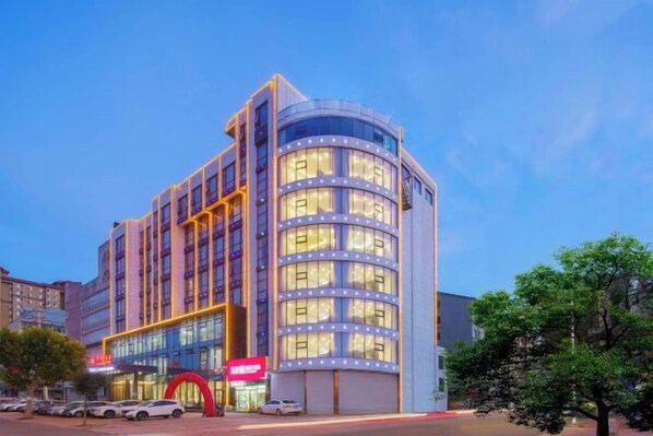 A multi-story hotel with a curved facade, large windows, and a prominent red archway at the entrance. - Zhuanghe Hualin Hotel (Zhuanghe)