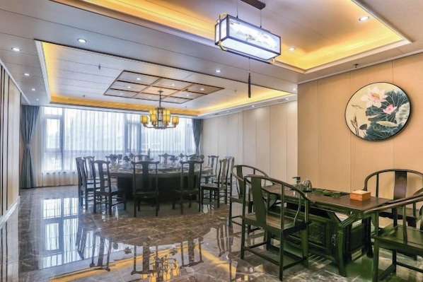 Un comedor de hotel con una mesa redonda, sillas, una araña y un cuadro grande en la pared.